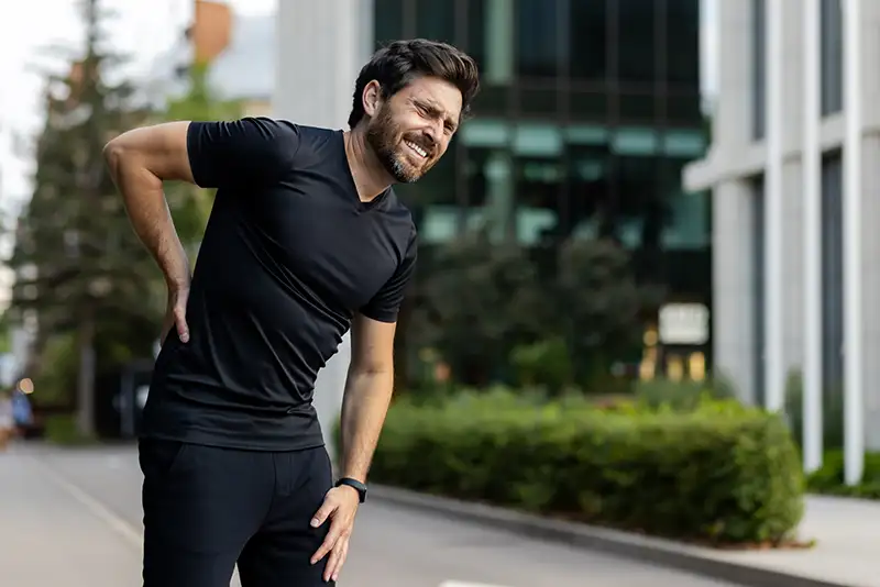 Man holding lower back in pain while standing outdoors, illustrating herniated disc symptoms