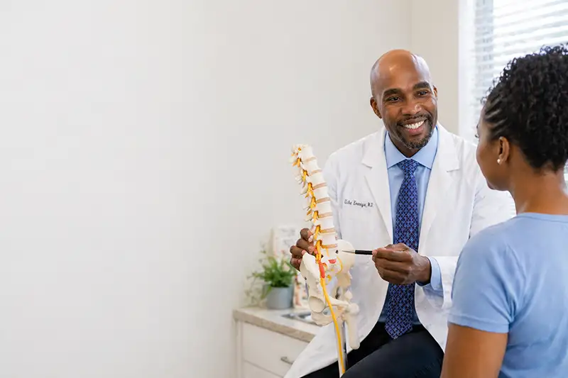 Dr. Uche Eneanya explaining sciatic nerve pain and radiculopathy to patient using spine model