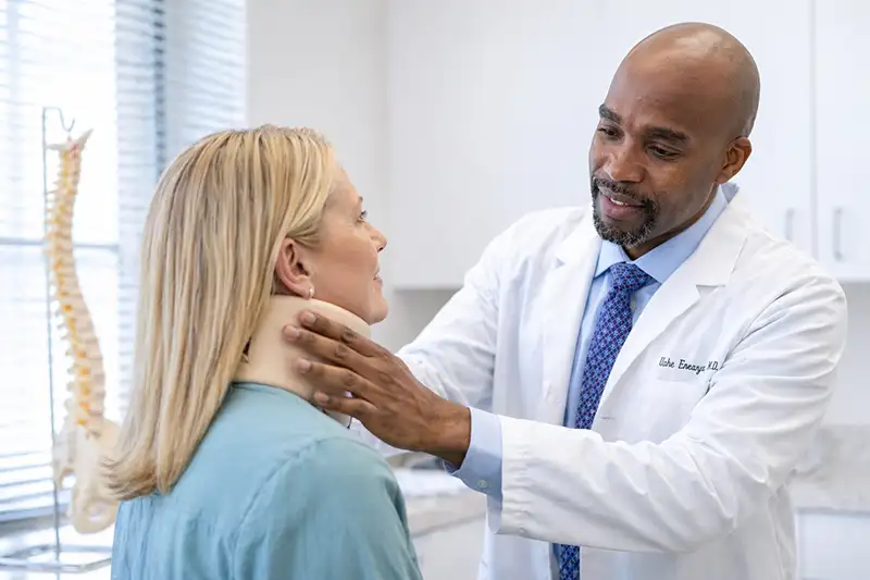 Dr. Uche Eneanya evaulating female patient with neck brace who has neck pain