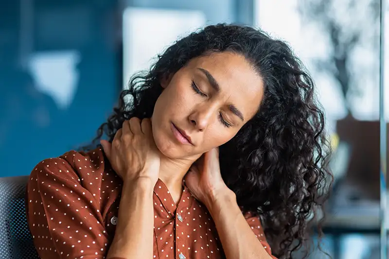 Woman holding neck in pain while sitting at desk, illustrating common neck pain symptoms
