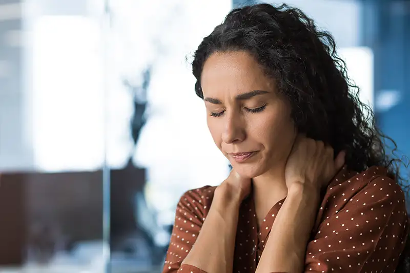 Woman experiencing neck pain and muscle tension while sitting at desk