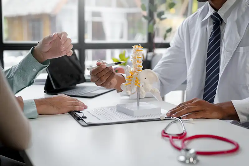 Physician explaining spine structure with model during back pain evaluation