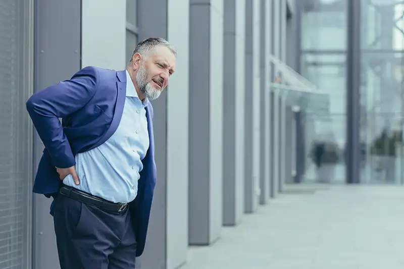 Man holding lower back in pain while standing outdoors