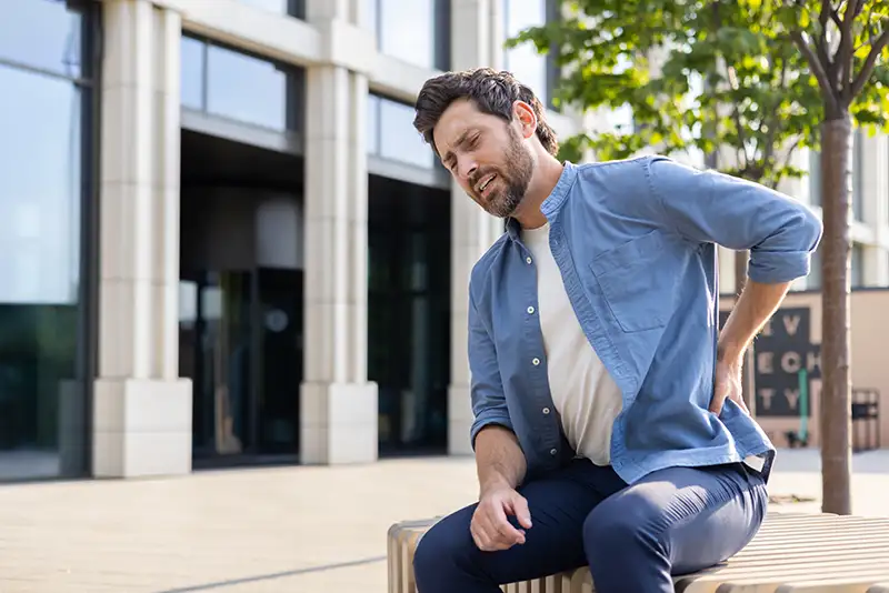 Man experiencing lower back pain while sitting outdoors