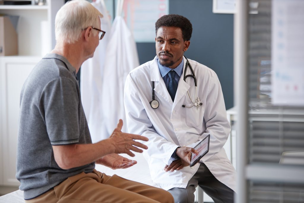 Doctor listening to an older male patient during a spine surgery consultation.